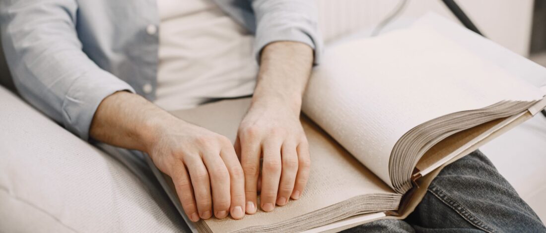 An adult reading a braille book indoors, highlighting visual impairment awareness.