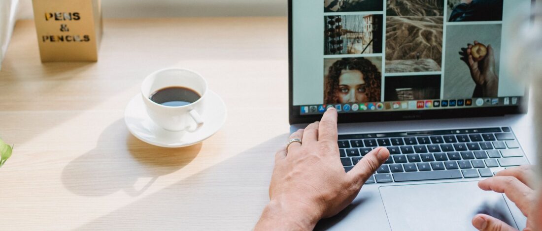 Crop anonymous male searching photos on internet using netbook while drinking coffee at table