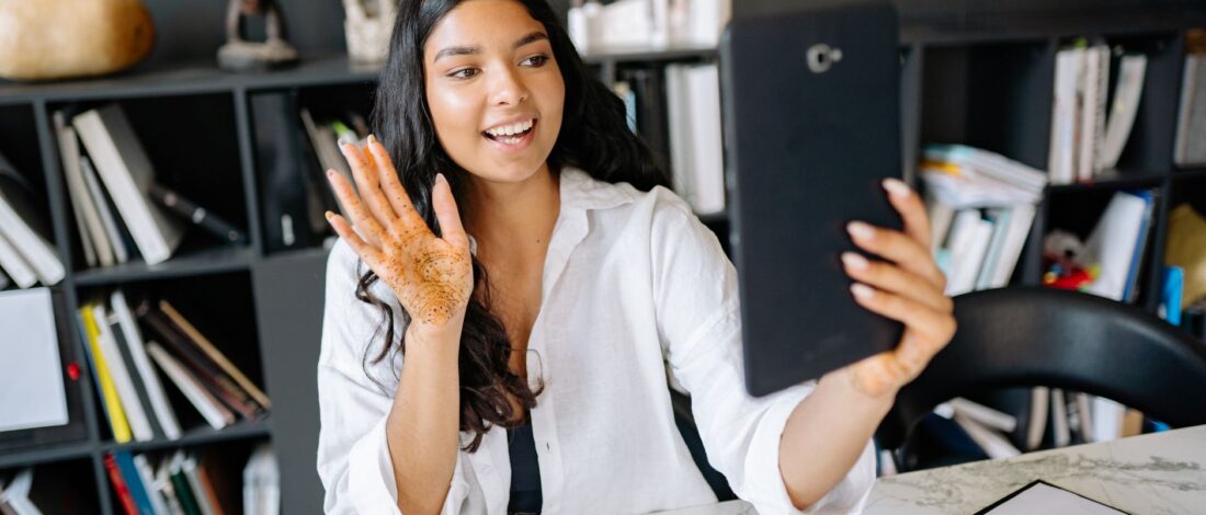 A young woman with henna on her hand video calling using a tablet in a modern office setting.