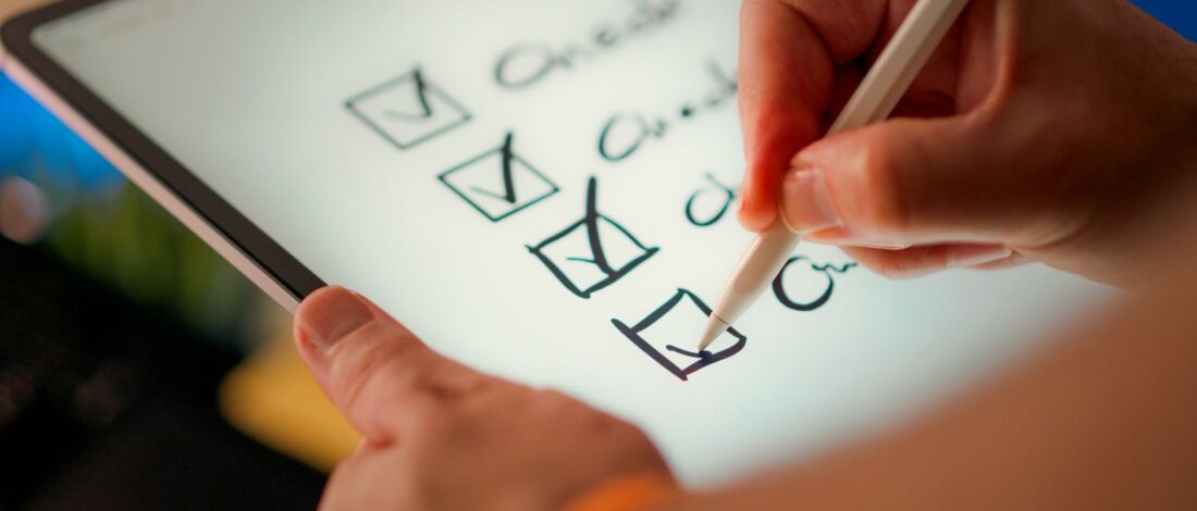 Close-up of a digital checklist being marked off on a tablet with a stylus pen.